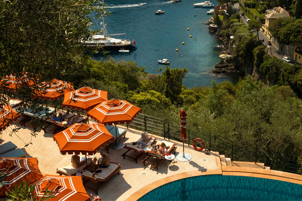 Bright orange umbrellas and sunbeds on a terraced beach platform above the cove