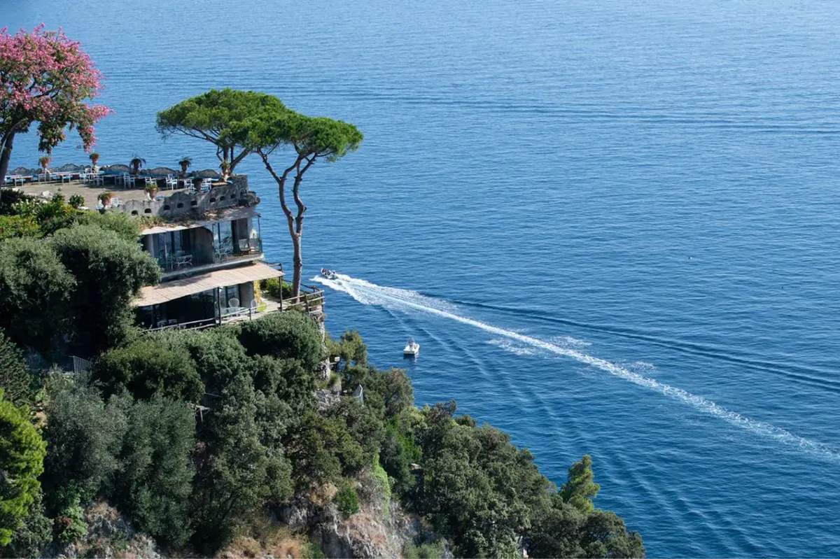 Cliffside building above Mediterranean water with native vegetation and umbrella pines