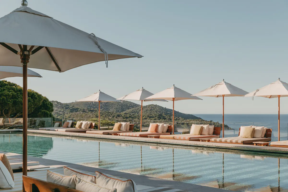 Pool deck with striped umbrellas and lounge chairs facing sea at sunset