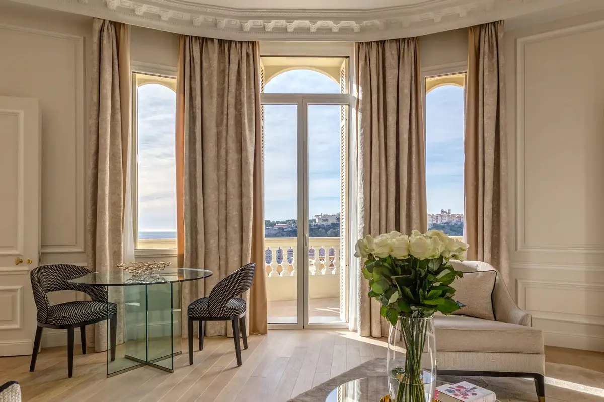Sitting area with arched glass doors opening to Mediterranean panorama, neutral tone furniture