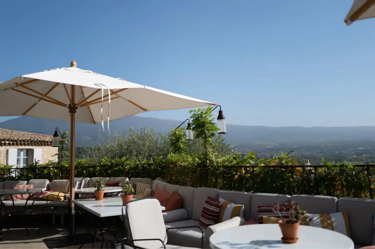 A terrace dining area with white umbrella, mountain views, and table seating with landscape backdrop