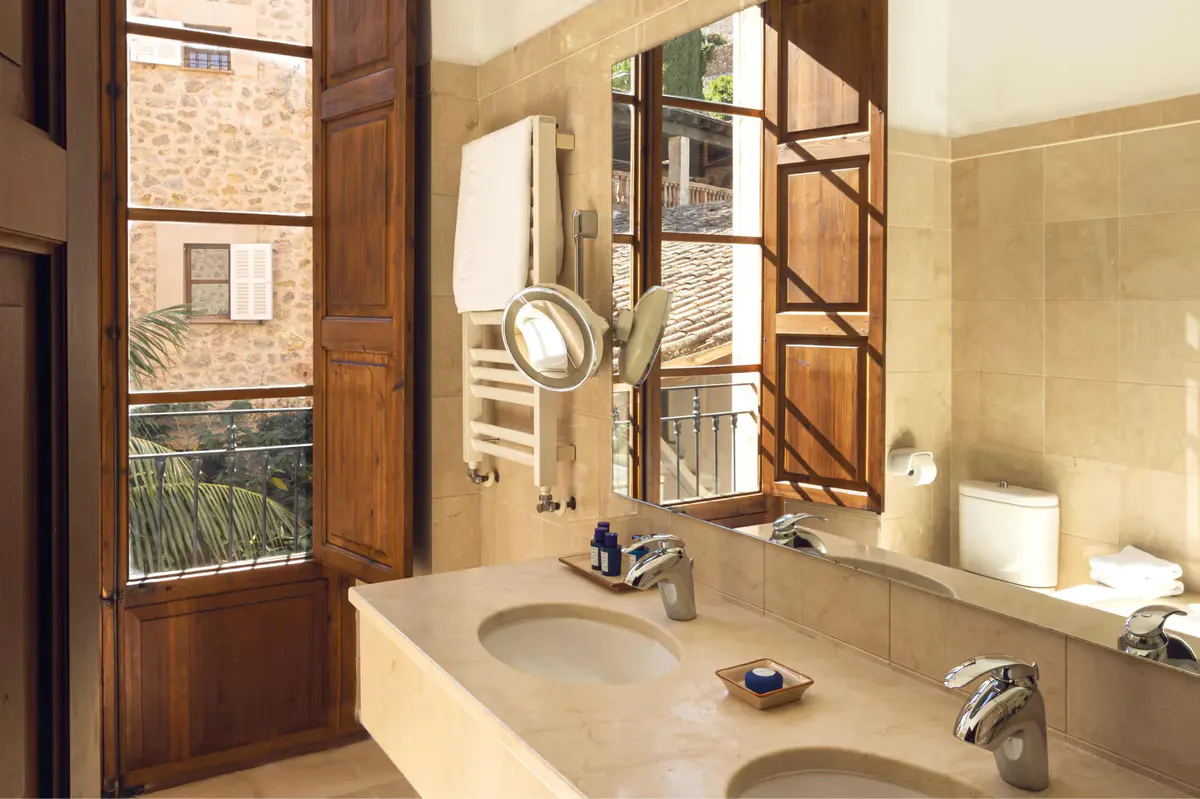 Bathroom with double sink vanity, wooden doors, framed mirrors, and view to village landscape