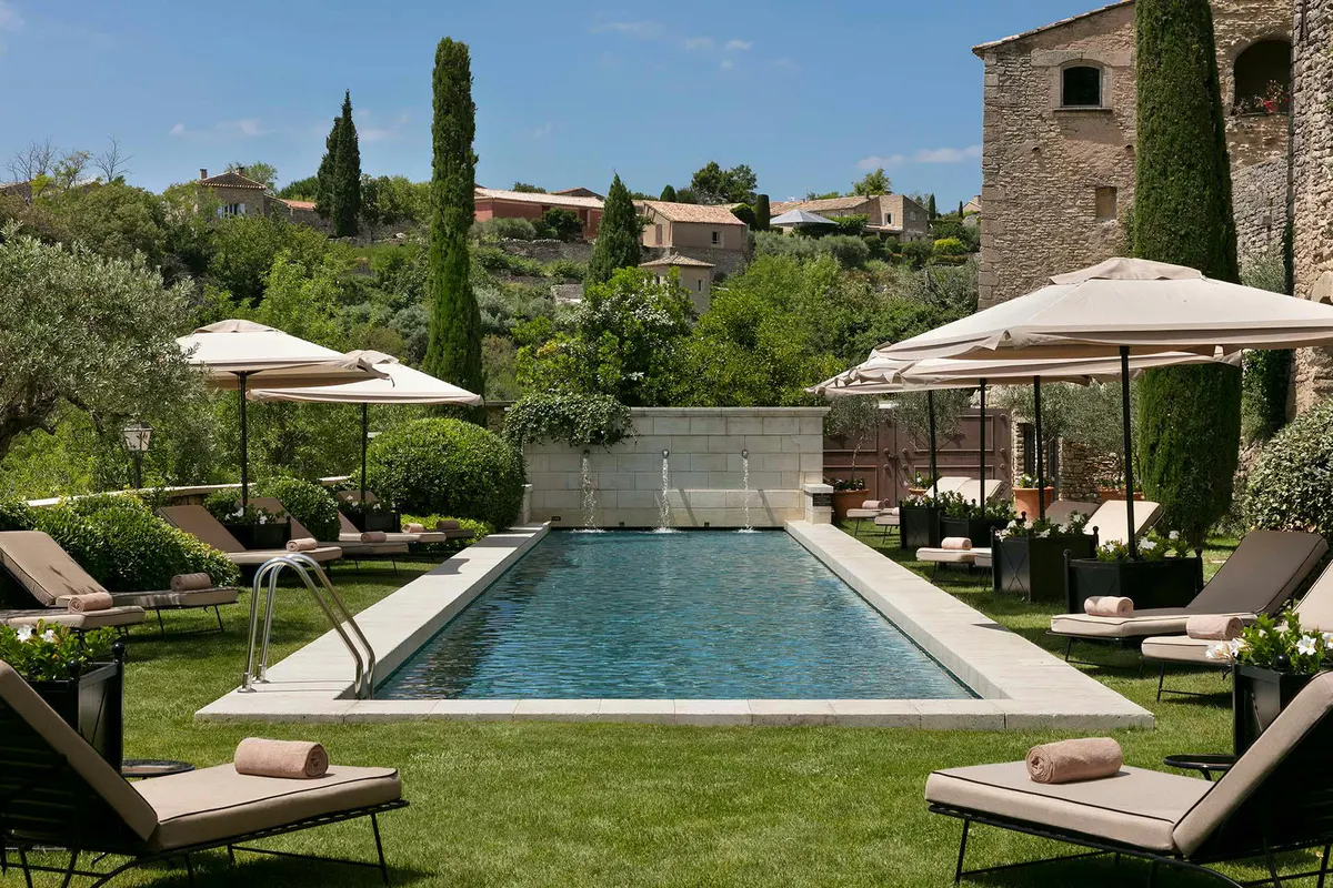 Rectangular pool lined with loungers and white umbrellas surrounded by stone walls and cypress