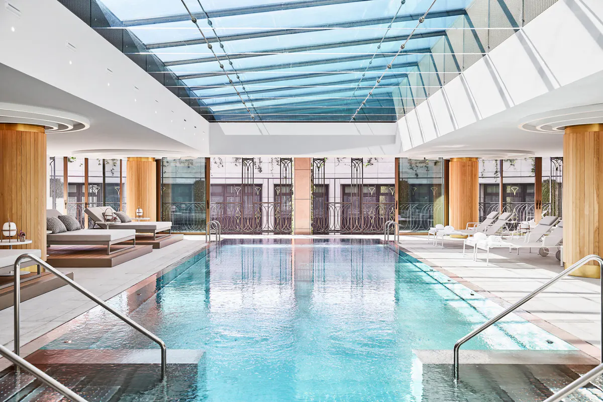 Indoor pool with glass skylight ceiling, white wood paneling, and lounging areas on both sides