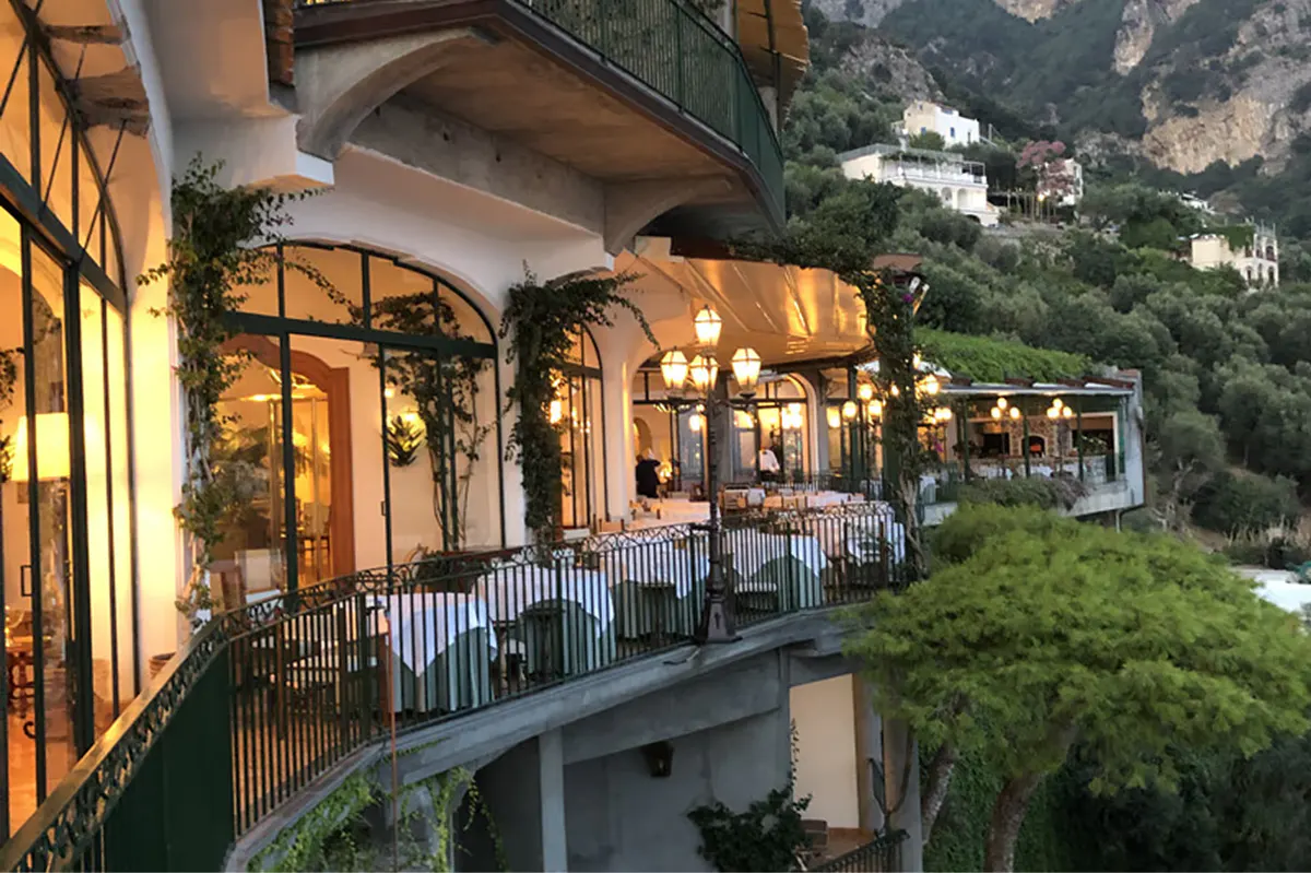 Evening-lit restaurant terrace with warm lighting, railings, and views across coastal town below