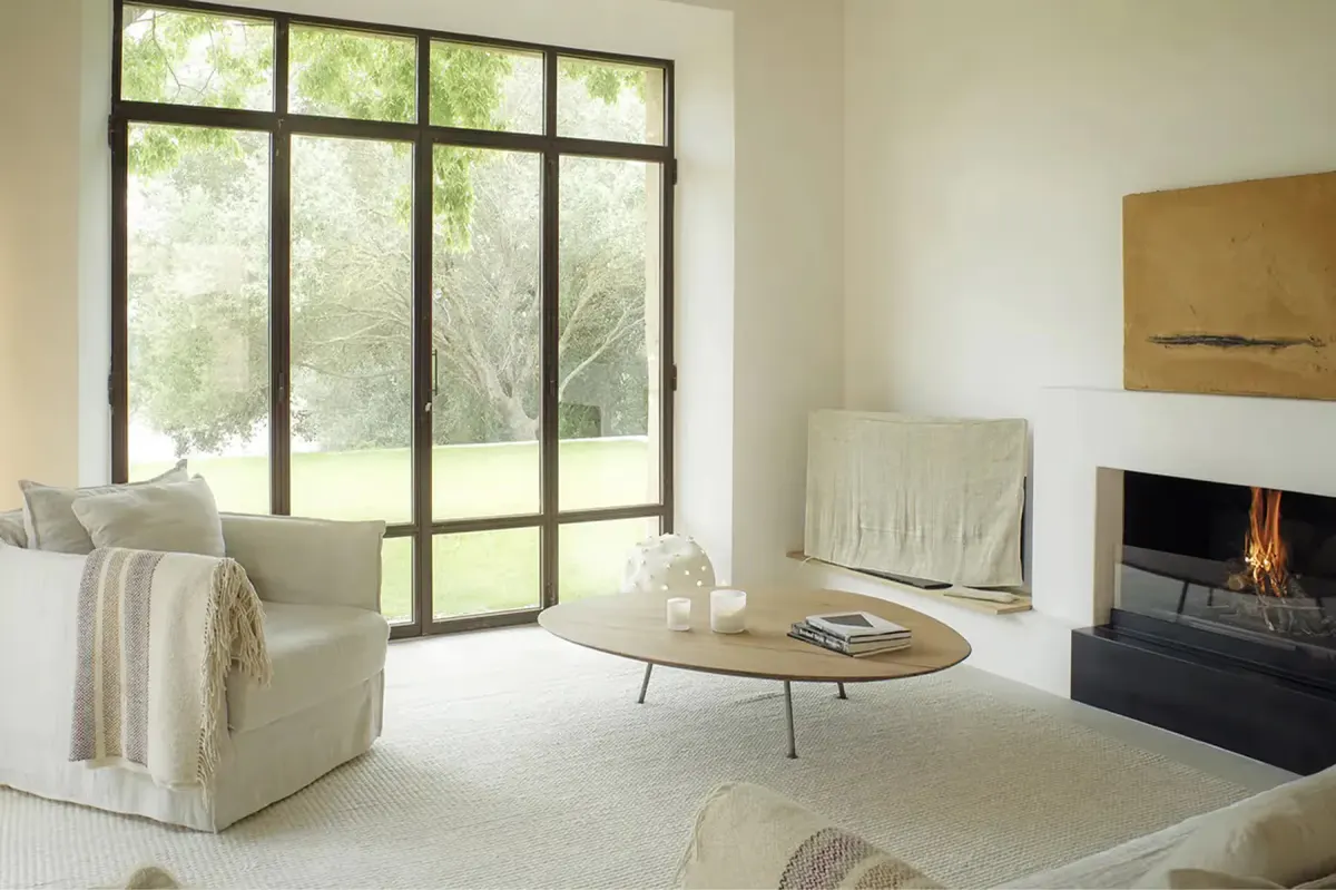 Contemporary living room with fireplace, metal-framed door wall opening to grounds, and light-toned furnishings