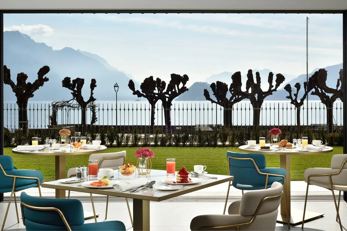 An outdoor terrace with tables set for dining, overlooking mountains and lake