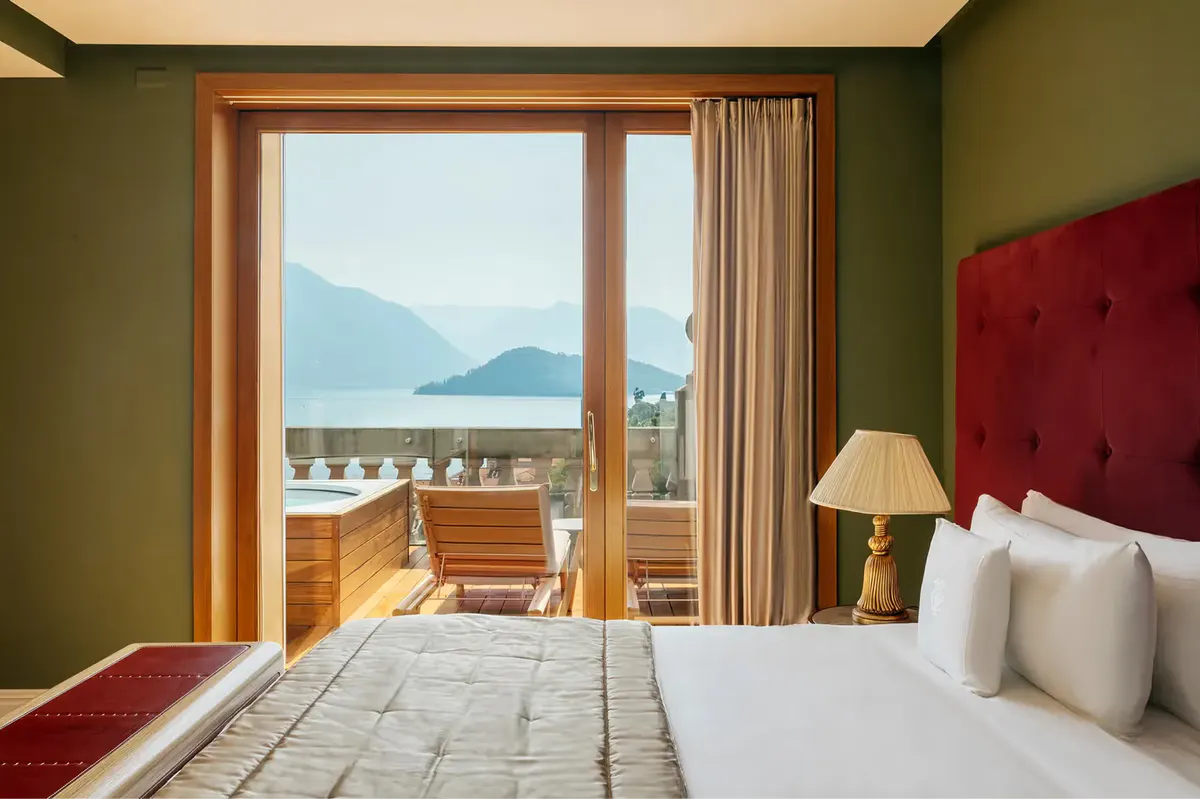 Bedroom with red headboard, wood doors opening to balcony with lake view