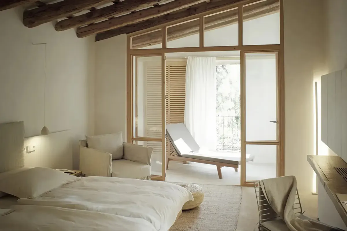 Serene minimalist bedroom with natural light from large windows, exposed wooden beams, and neutral linens