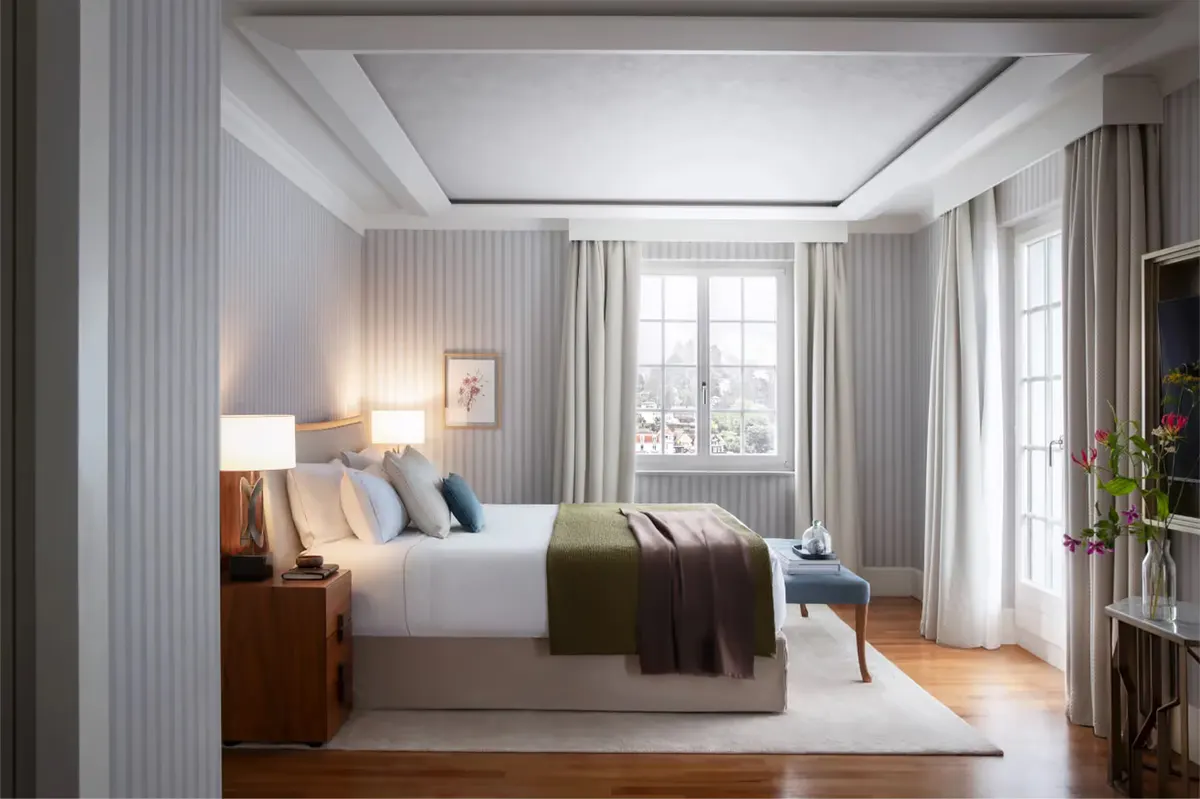 Light-filled bedroom with striped pale walls, white coffered ceiling, layered linens, and tall windows opening to landscape