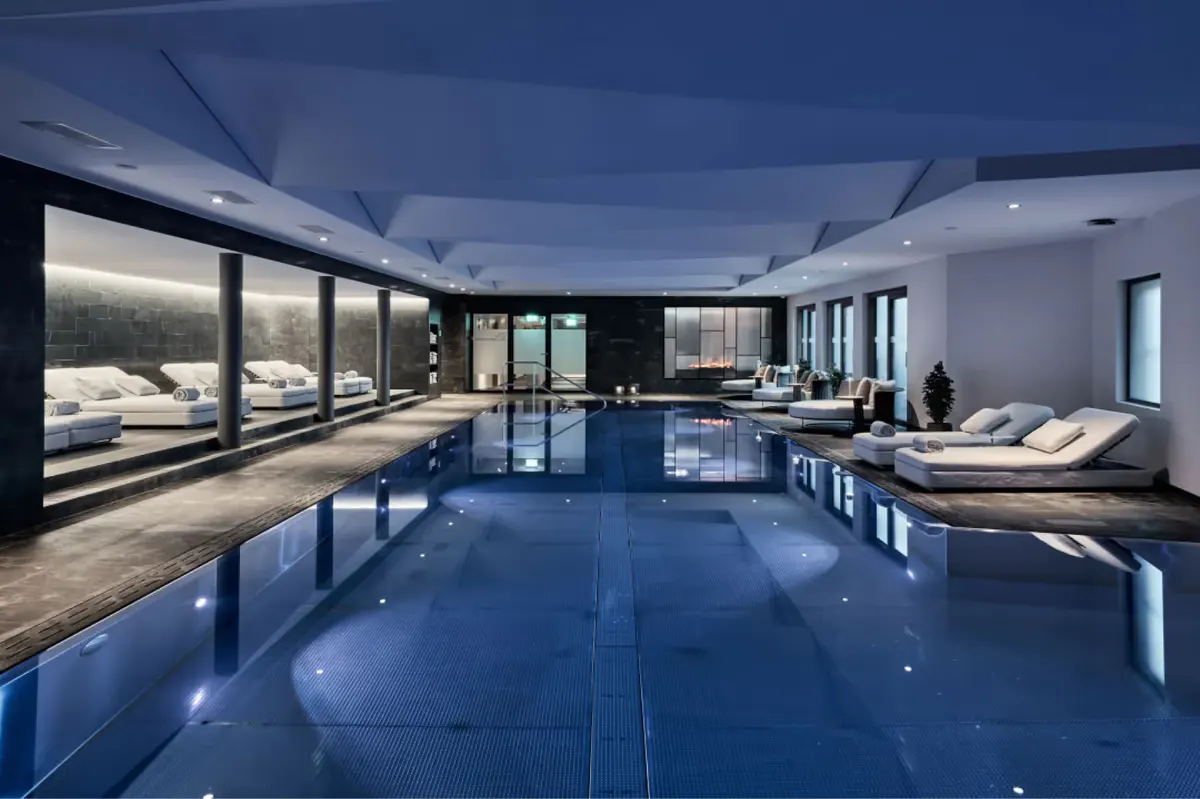 Large indoor pool with glass ceiling, loungers, and sweeping alpine mountain views