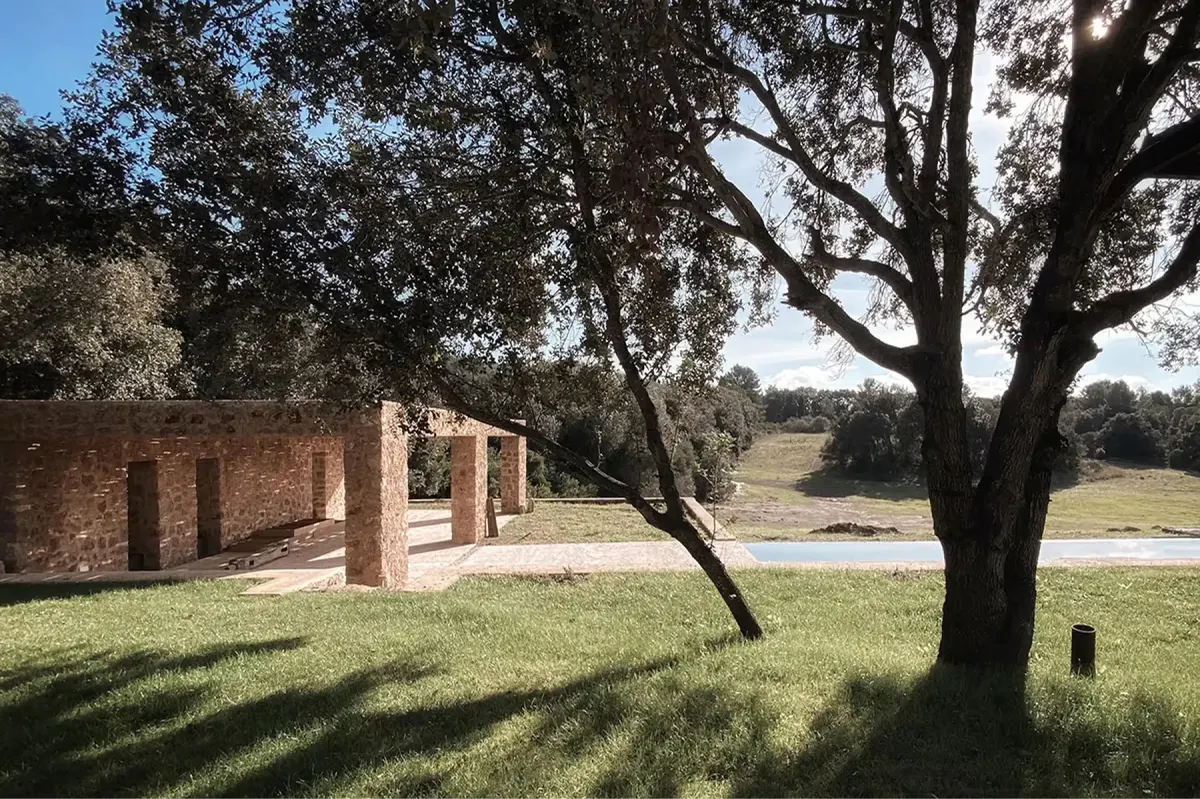 Stone building with rounded archway entrance situated within grassy estate with mature olive trees