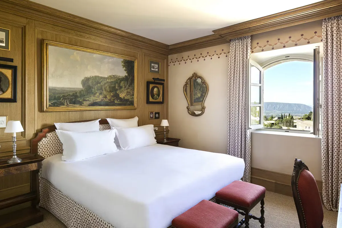 Bedroom with pale yellow walls, white bedding, red accent pillows, and valley views