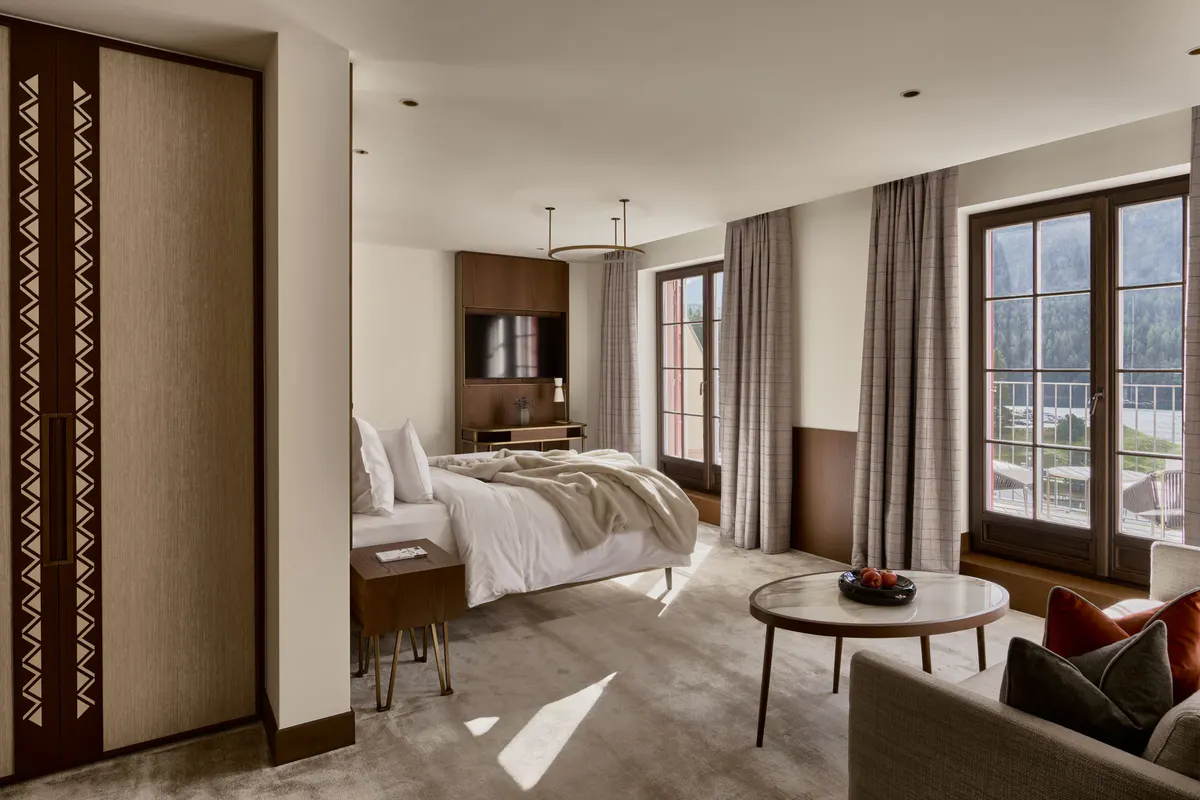 Bright bedroom with white bedding, wooden built-ins, and glass doors to mountain-view terrace