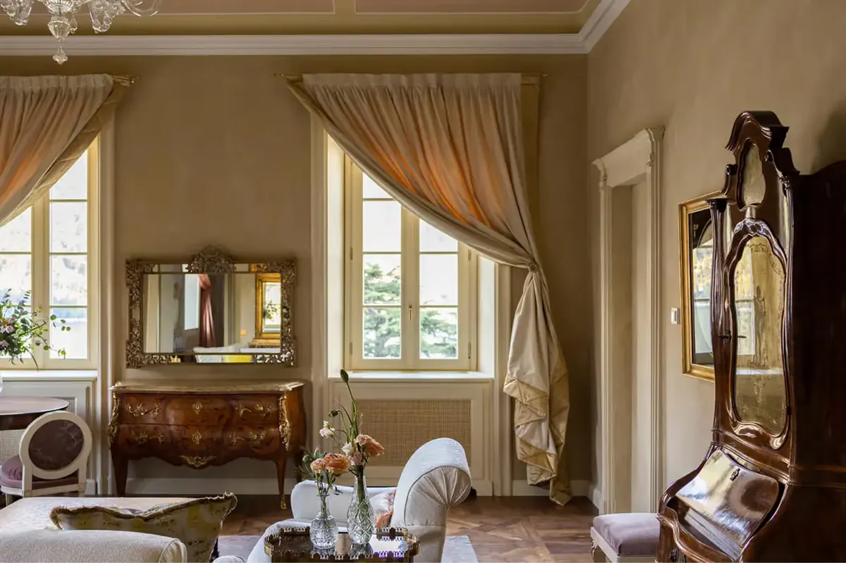 A bedroom with cream walls, ornate desk, and fabric draping from gilded cornice