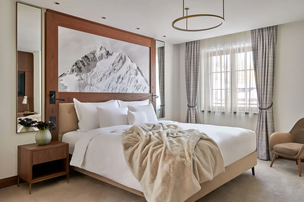 Suite bedroom with wood headboard, cream bedding, and artwork above alpine views