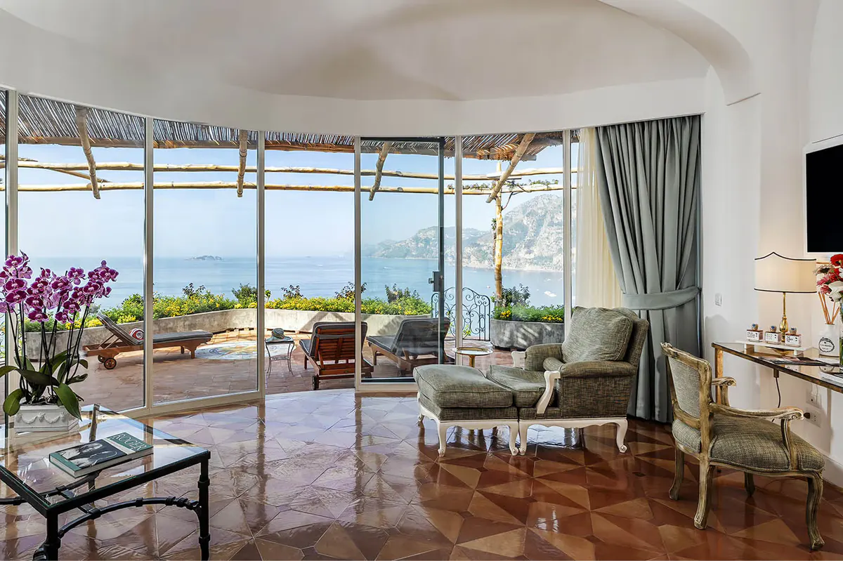 Suite interior with curved ceiling, window seating, terrace access, light curtains, and sea vistas