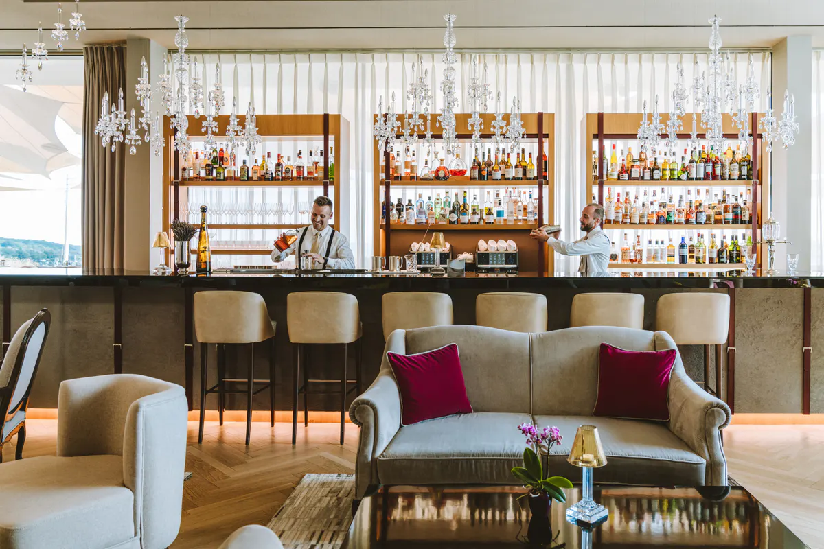 Modern bar with extensive shelving, wine bottles displayed, and upholstered bar seating