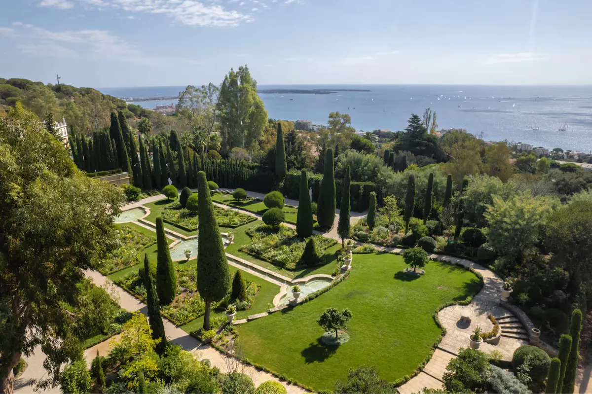 Rectangular pool overlooking sea, lined with cypress trees and sun loungers on paved terrace