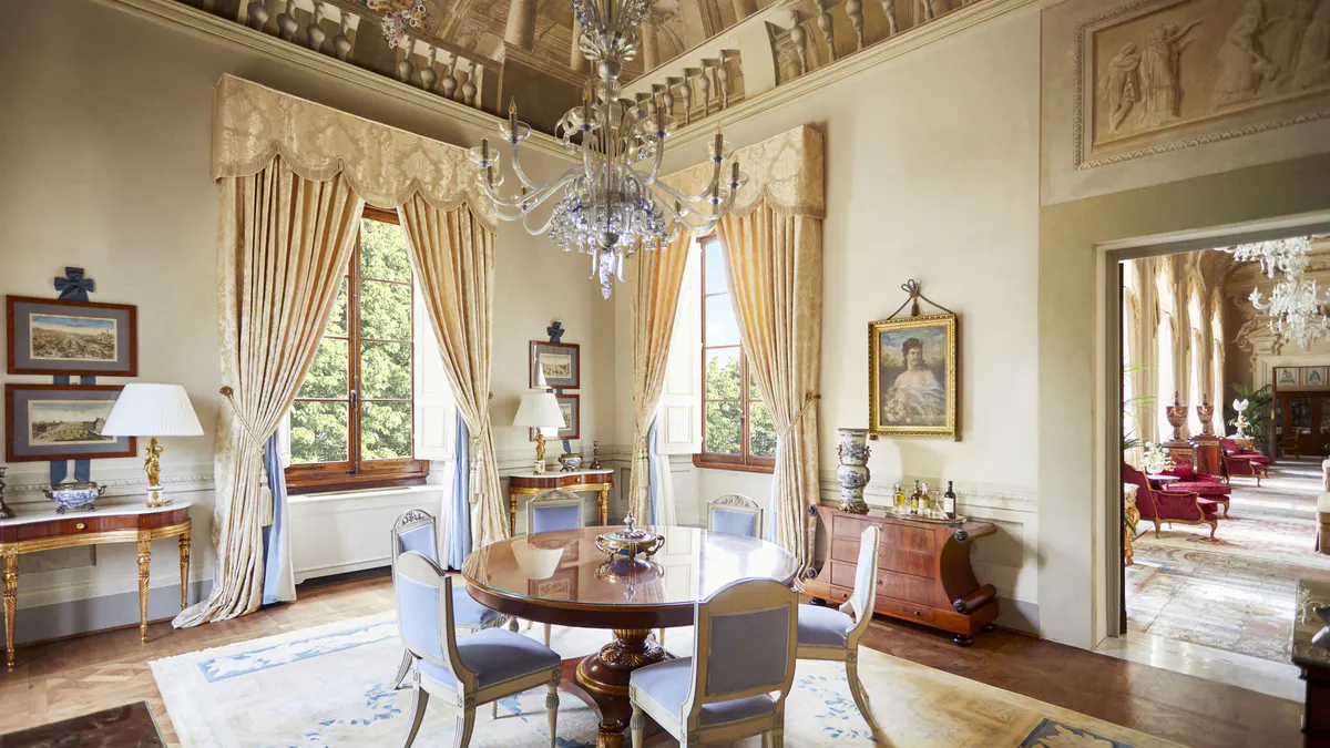 High-ceilinged sitting room with tall windows, yellow silk damask drapery, and classical furnishings