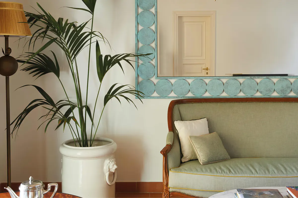 Living area with pattern-accented walls, potted palm plant, cream furnishings, and contemporary art