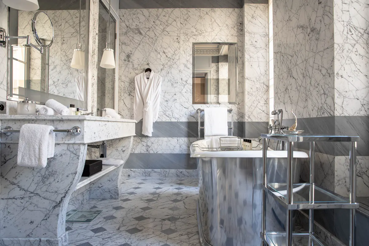 A marble bathroom with multiple mirrors, brass fixtures, and white towels