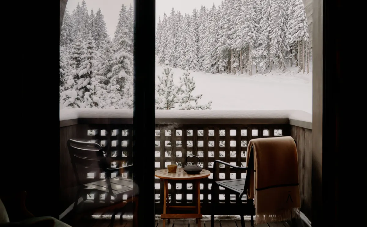 Private balcony with armchairs, a side table, and a wool blanket overlooking snow laden pines