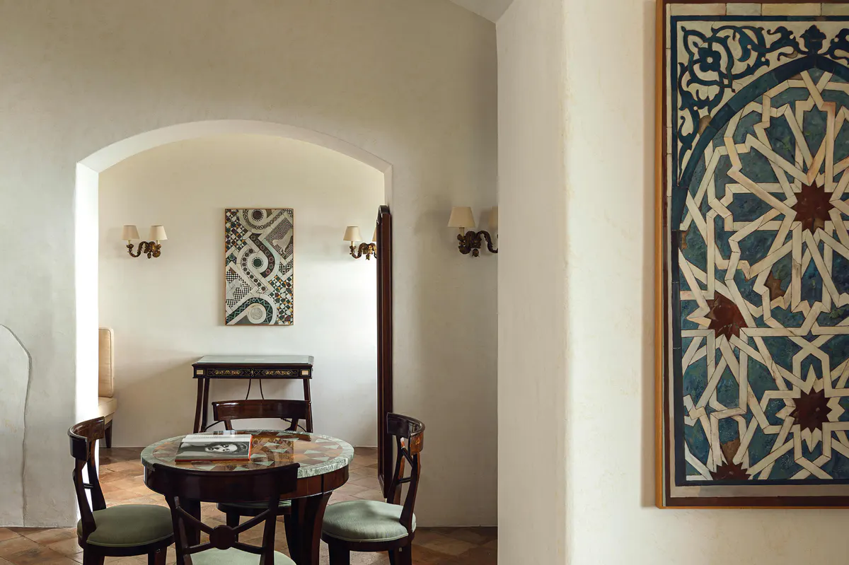 Gallery space with arched alcove, patterned wall art, round black table, and green upholstered seating