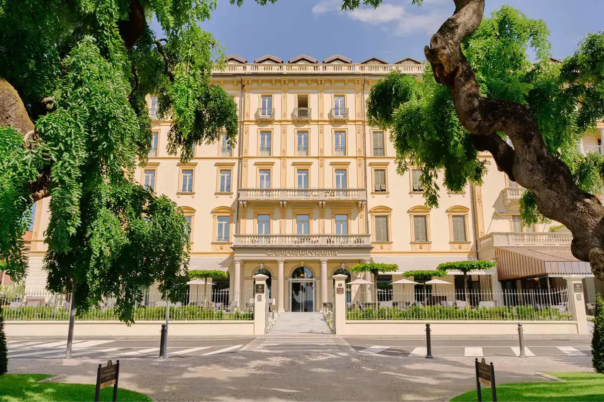 The hotel’s cream and gold facade with a formal plaza and small trees in front