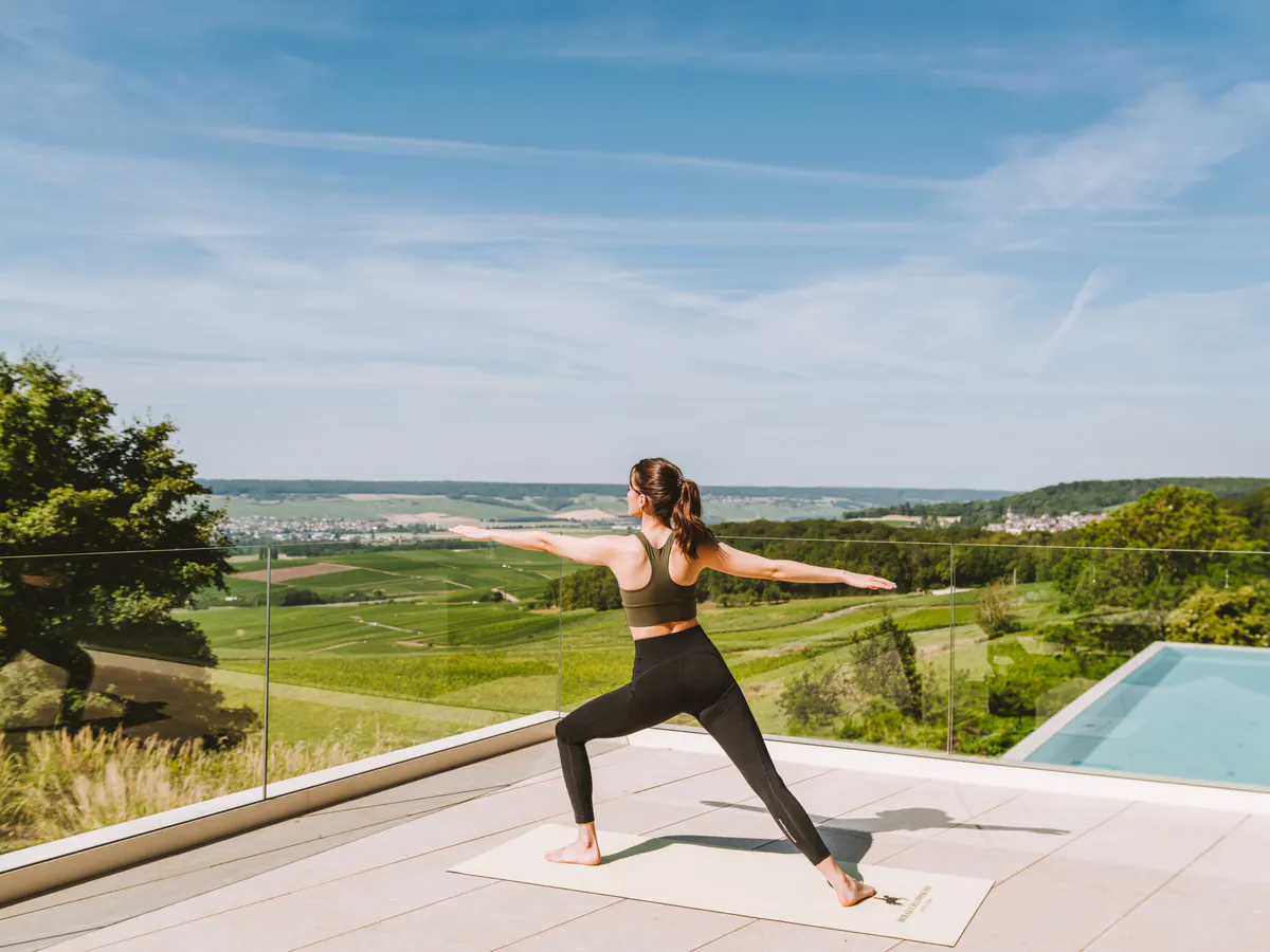 Woman in yoga pose on terrace overlooking rolling vineyards and distant valleys