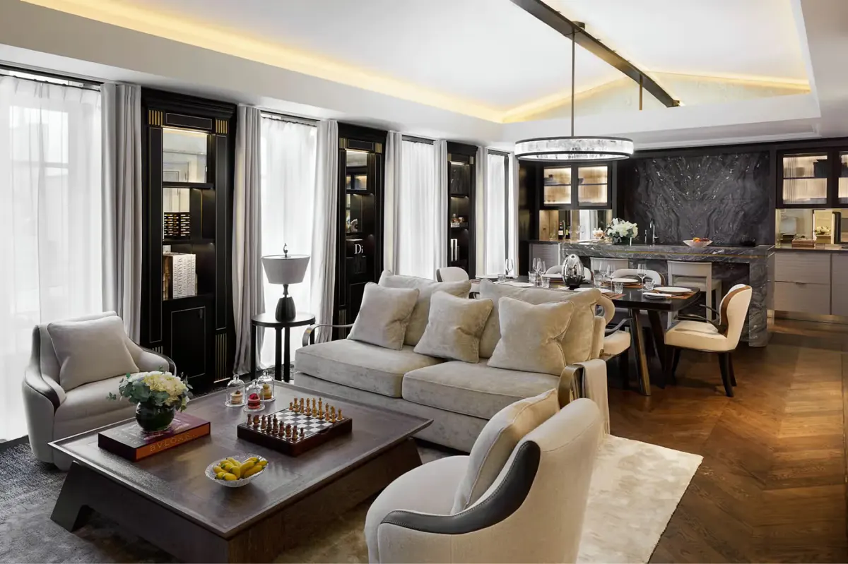 A suite living area with gray sofa, dark coffee table, and pale armchairs near bright windows