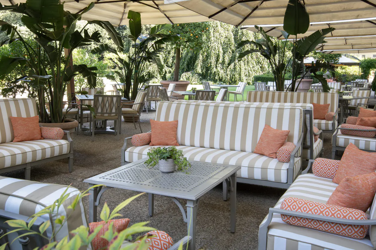 Garden dining pavilion with striped lounge seating, tropical plants, and orange cushions