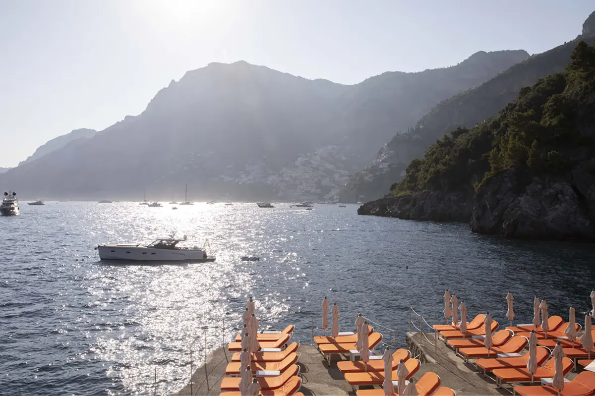 Cove with striped lounge chairs overlooking sparkling Mediterranean water and distant mountains