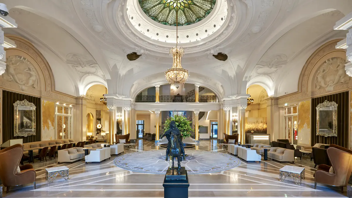 Grand lobby with painted ceiling dome, marble floors, gilt arches, and skylight