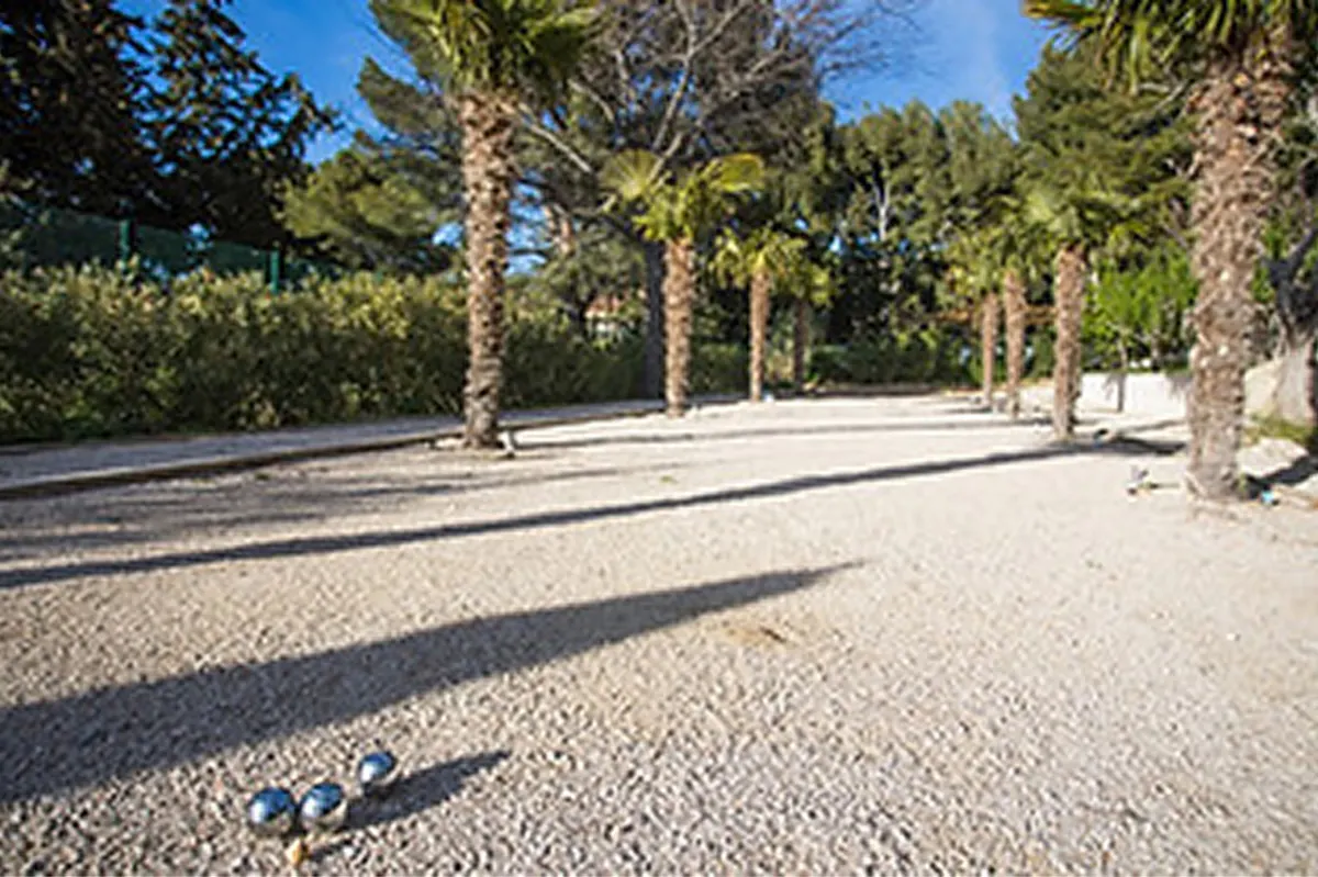 Paved courtyard with tall stone column shading, palm trees, and surrounding stonework