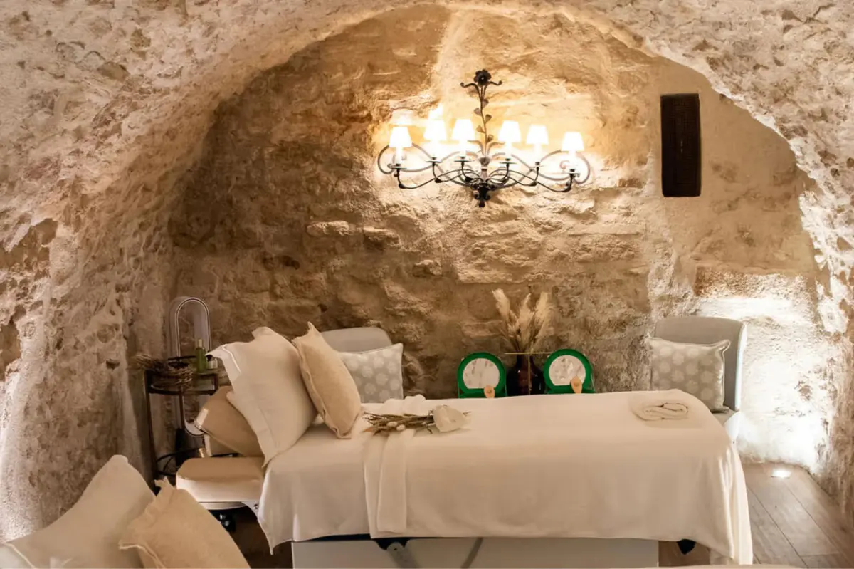A spa treatment room carved into stone with arched ceiling, massage table, and soft ambient lighting