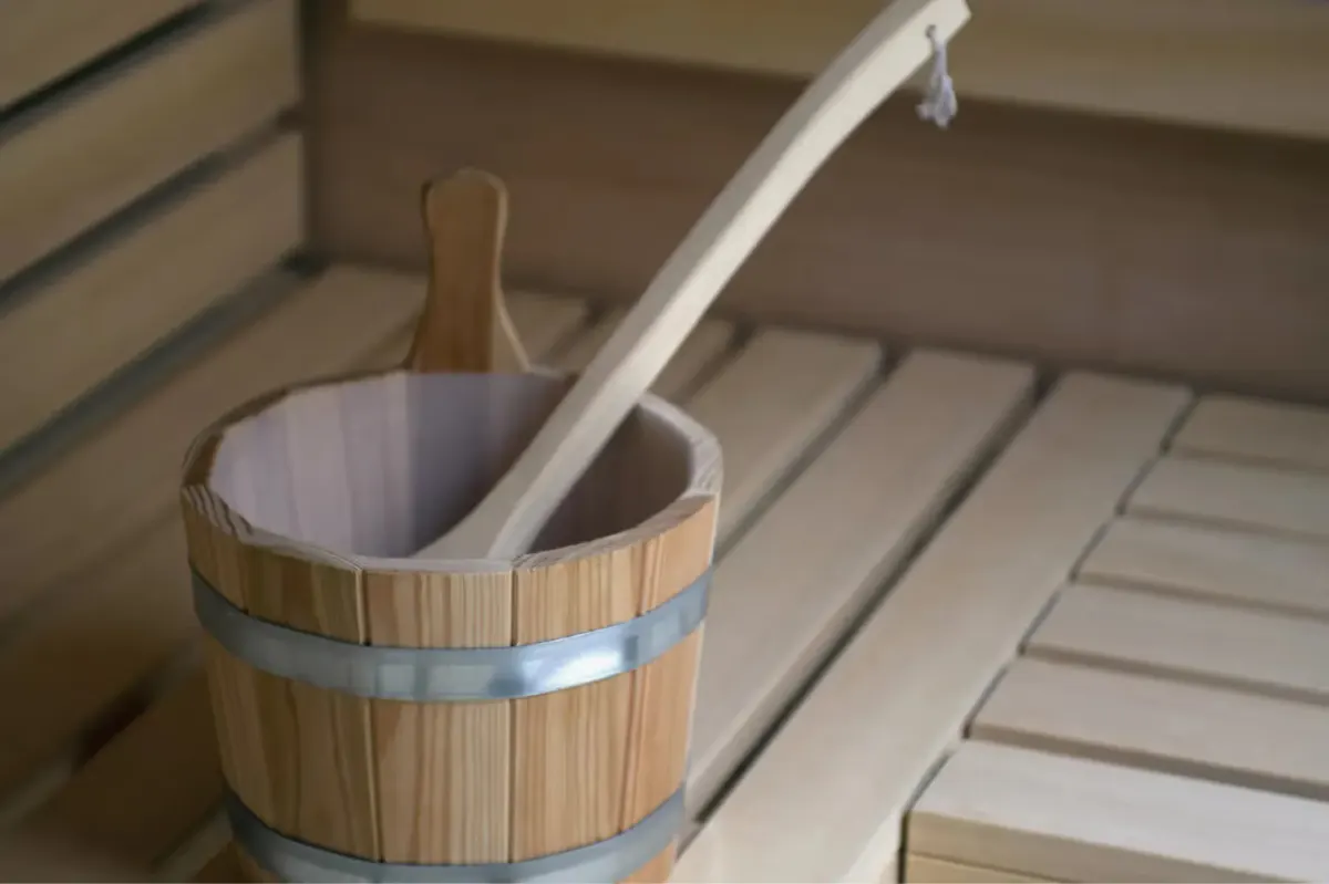 Wooden sauna bucket with ladle resting on slatted bench seating