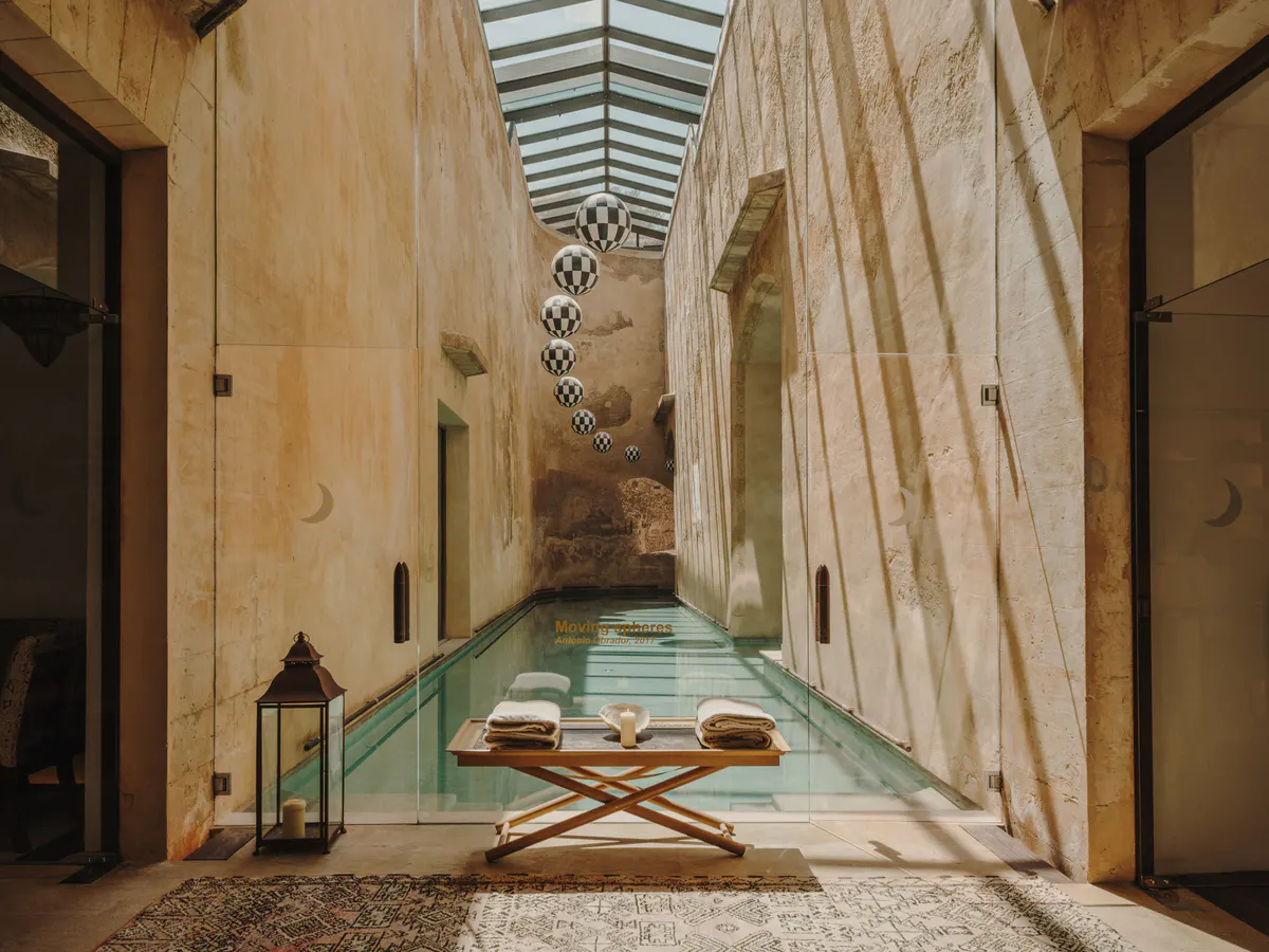 A spa corridor with turquoise pool, smooth stone walls, wooden columns, and glass skylight