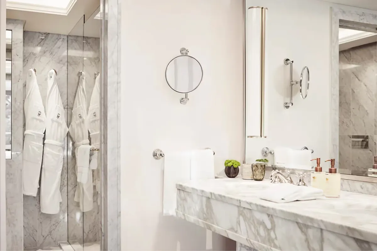 A marble bathroom with dual sinks, mirrored walls, and glass shower enclosure
