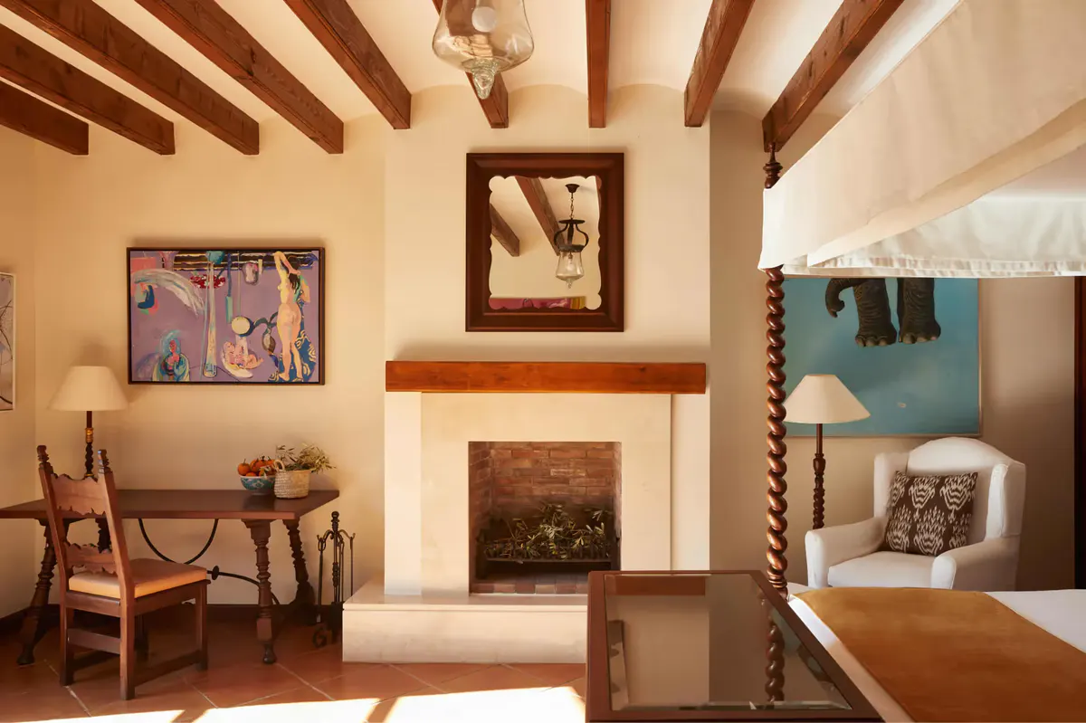 Living room with fireplace, exposed wooden beams, colorful artwork, and doorway opening to terrace