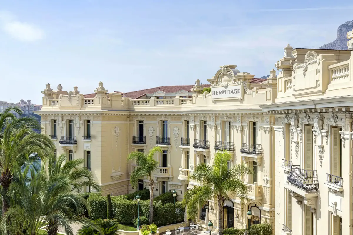 Pale stone façade with arched windows and columned entry, tropical palms visible on square