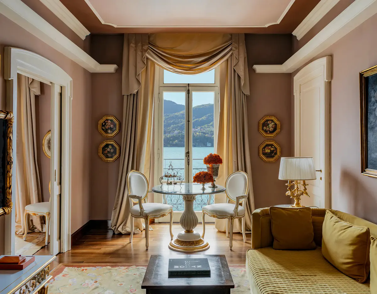 A suite room with draped windows, gold furnishings, and lake-view doors