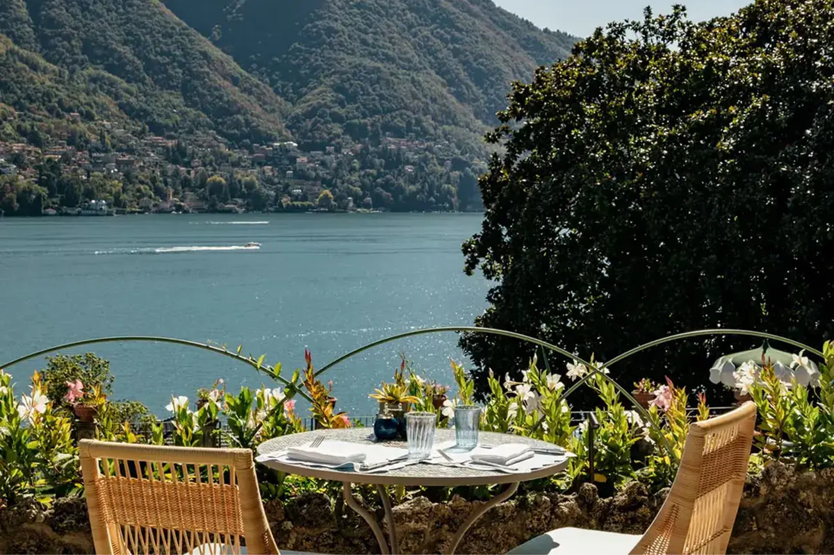 A terrace table with lake and mountains visible beyond flowering potted plants