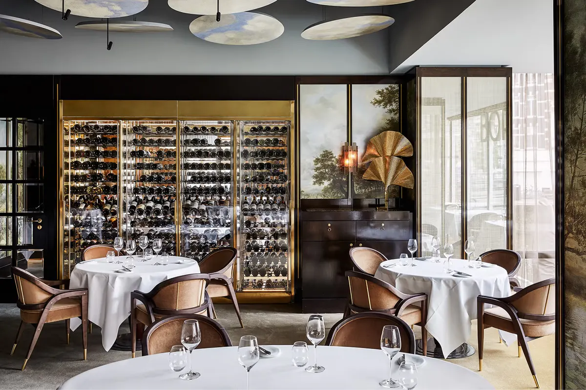 Contemporary dining space with glass wine cellar backdrop and minimalist table settings