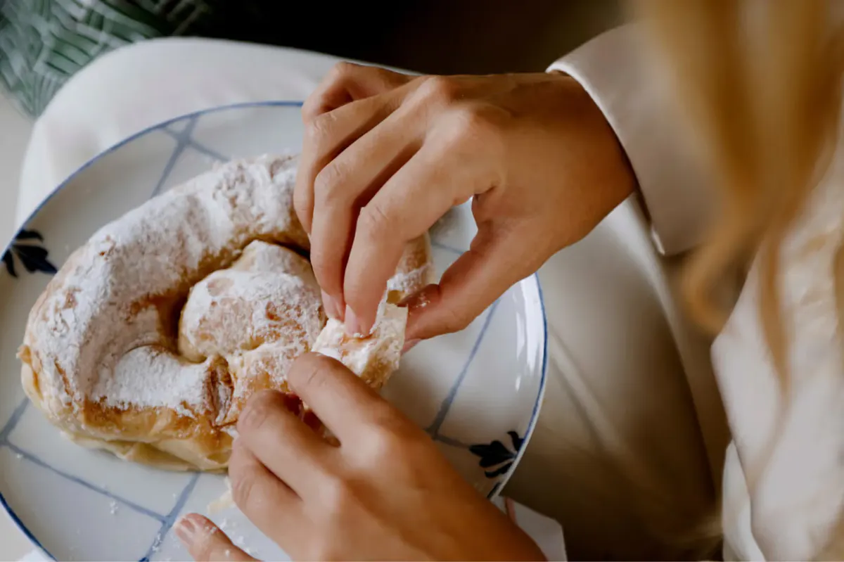 Hands breaking artisan bread over a white plate during meal