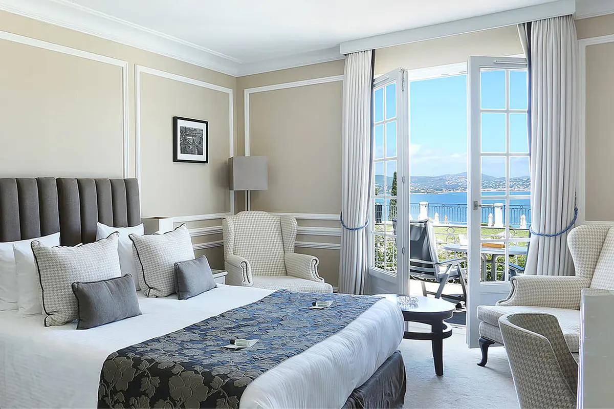 Bedroom with cream-colored upholstered headboard and windows onto Mediterranean views