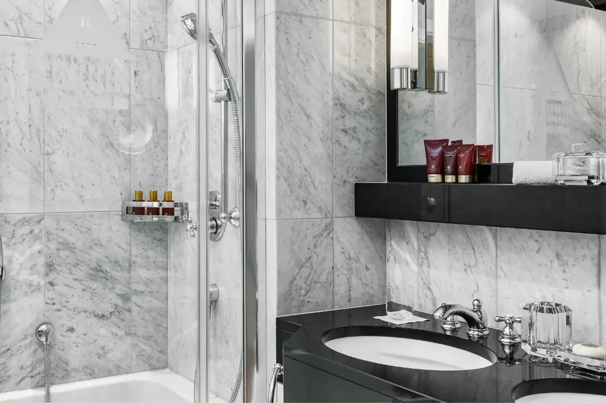 Bathroom with marble shower enclosure, black vanity, and brass accessories
