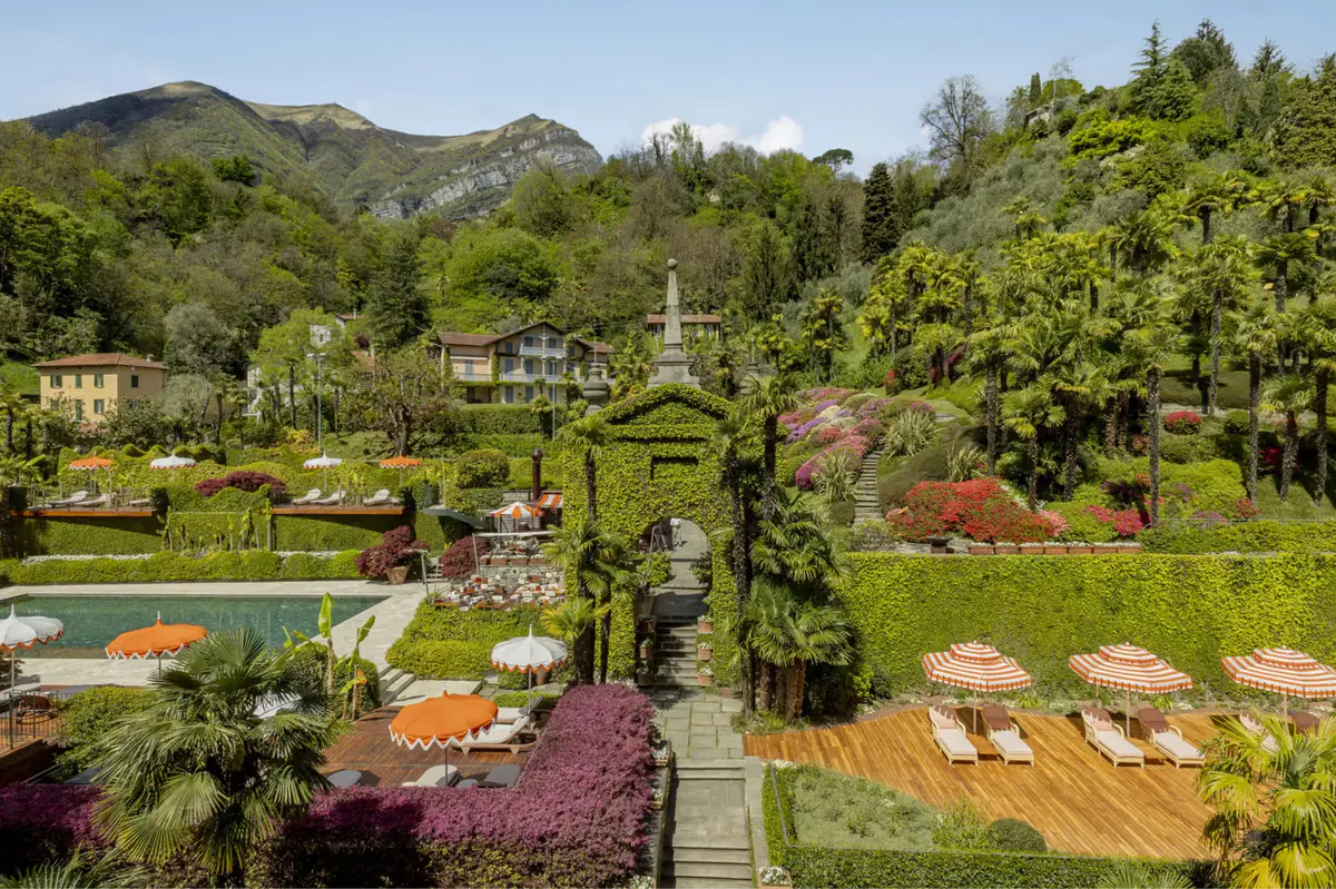 Manicured gardens with flowering beds, a pond, and hotel buildings set in green hills