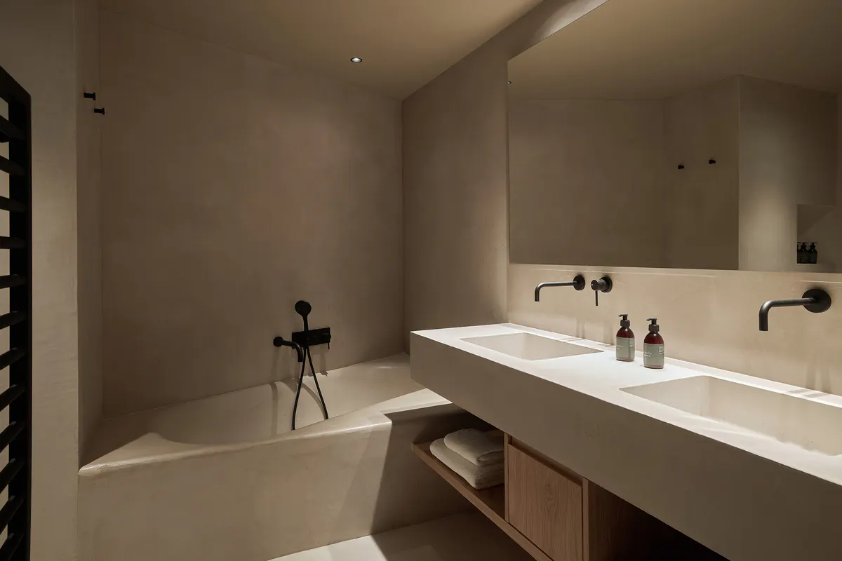A minimalist bathroom with concrete and natural wood vanity, white fixtures, and soft lighting