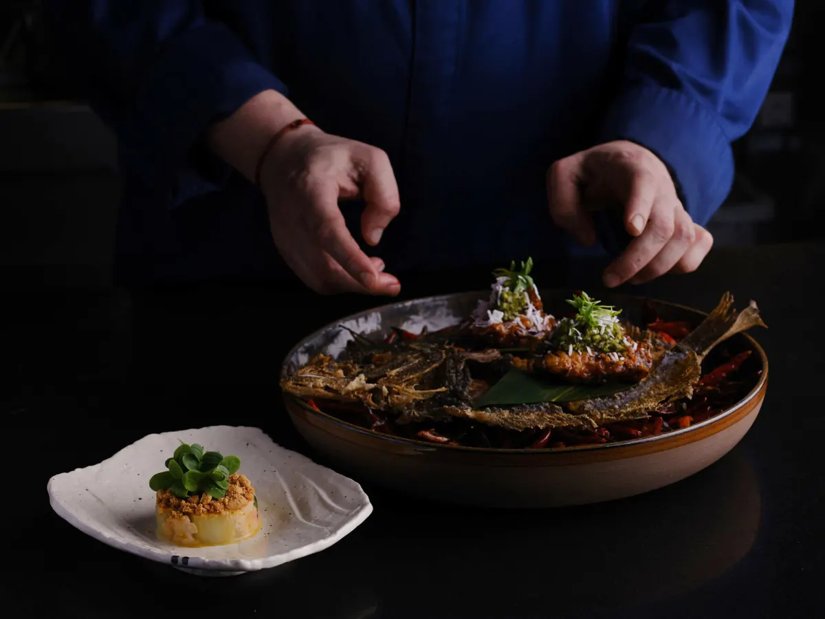 Pan-Asian seafood dish plated on slate with wooden bowl and garnish, hands presenting the plate